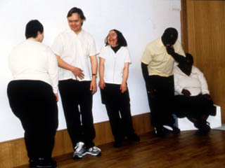 A row of dancers against a white wall in a gallery space smiling and wearing black & white costumes